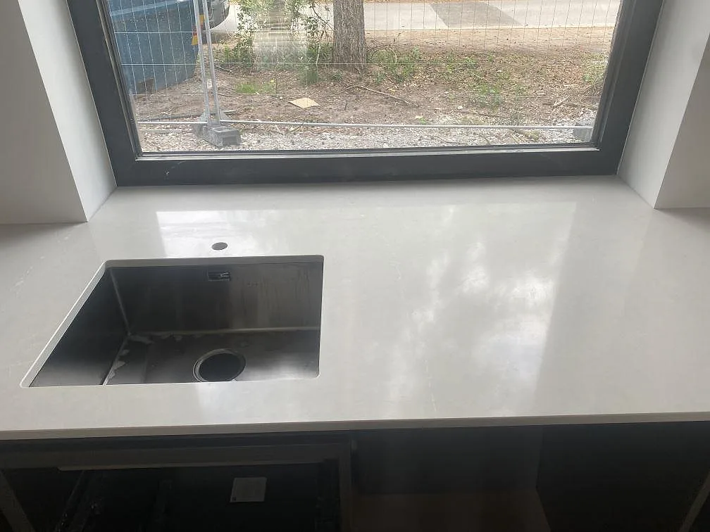 Polerad köksbänkskiva i Silestone Desert Silver med underlimmad rostfri diskho framför fönster i Höllviken.
