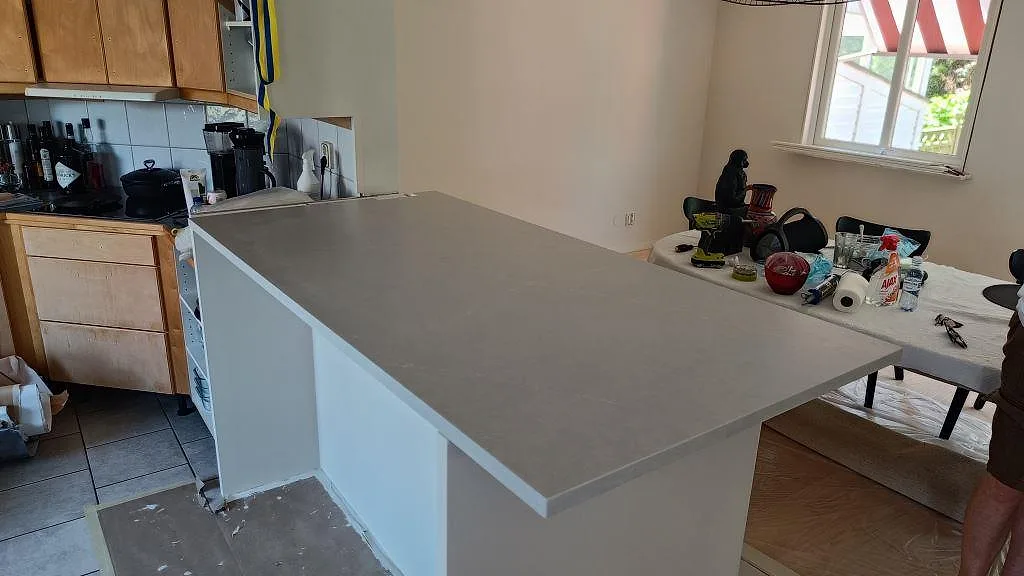 Köksbänkskiva i grå Silestone Desert Silver, matt Mocka, som bred halvö på vita stommar i ett kök i Hovås.