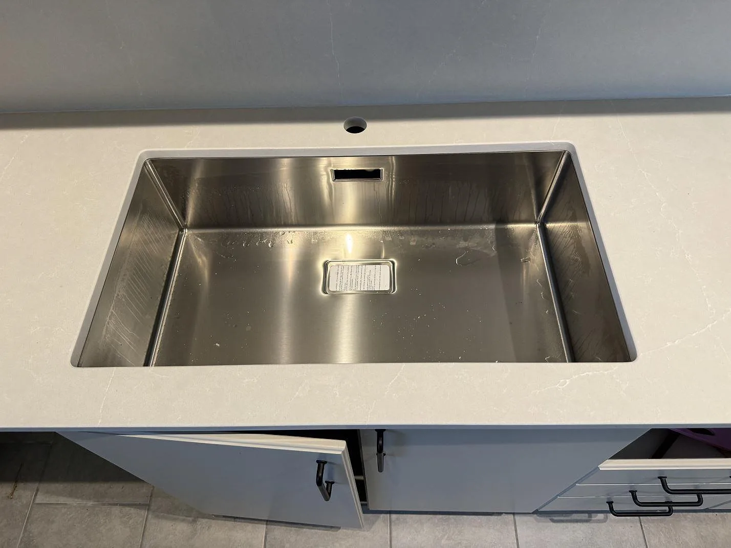 Närbild på underlimmad rostfri diskho i Silestone Desert Silver, Mocka, med ljus ådring i ett kök i Hovås.