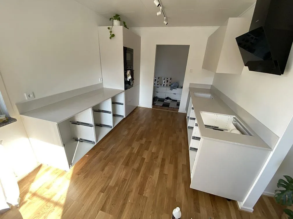 Köksbänkskivor i polerad Silestone Desert Silver med uppvikt stänkskydd längs två väggar i ett kök i Ingelstad.