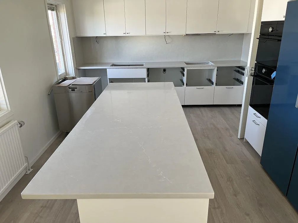 Stort kök i Jönköping med lång köksö i polerad Silestone Desert Silver och en väggrad med diskhoar och hälluttag, fotograferat under montering.