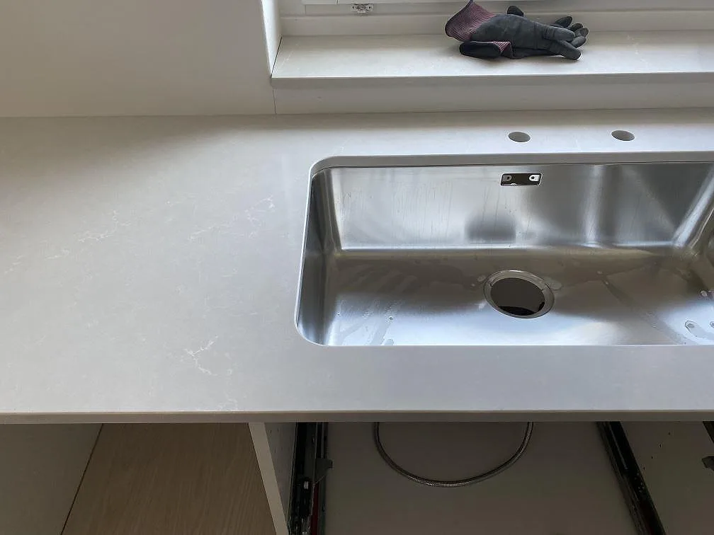 Närbild på polerad Silestone Desert Silver runt en underlimmad rostfri dubbelho under fönster i Karlshamn.