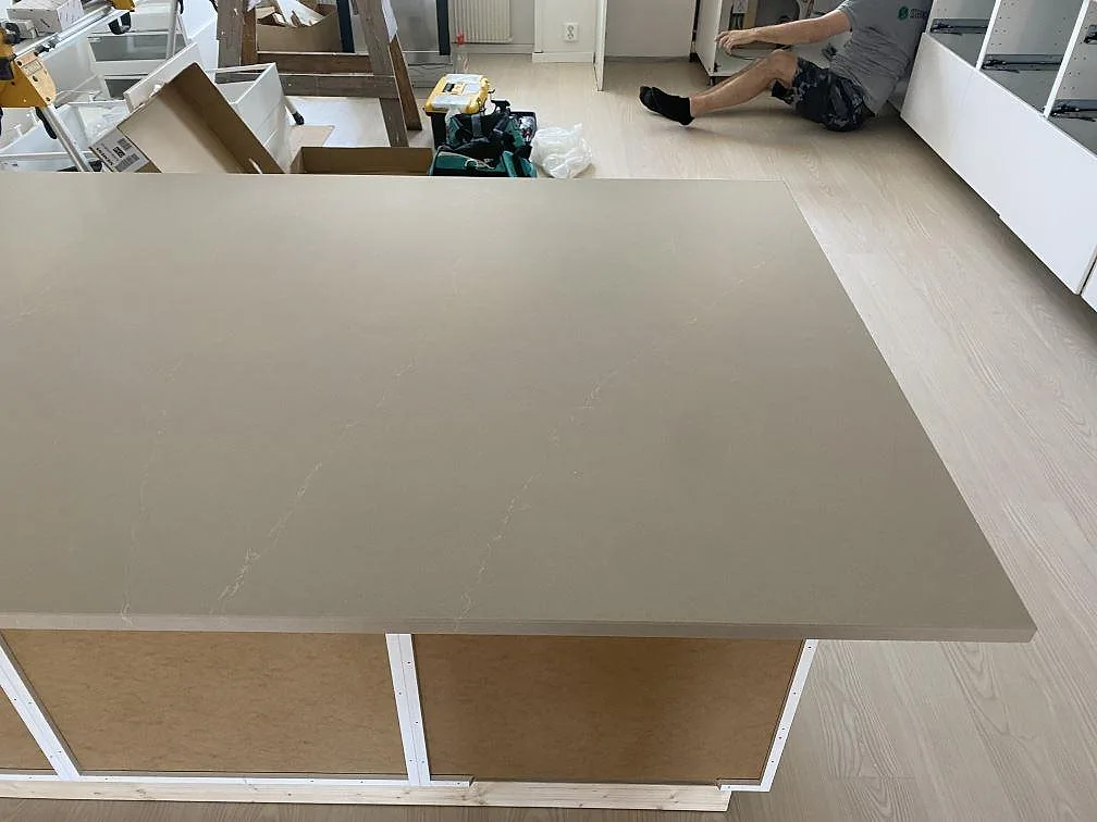 Köksbänkskiva i polerad Silestone Desert Silver med halvö och ljusa köksstommar under montering i Karlshamn.