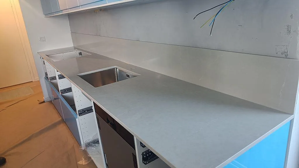 Köksbänkskiva i Silestone Desert Silver kvartskomposit, polerad, med rostfri diskho och stänkskydd i ett kök i Karlskrona under montering.