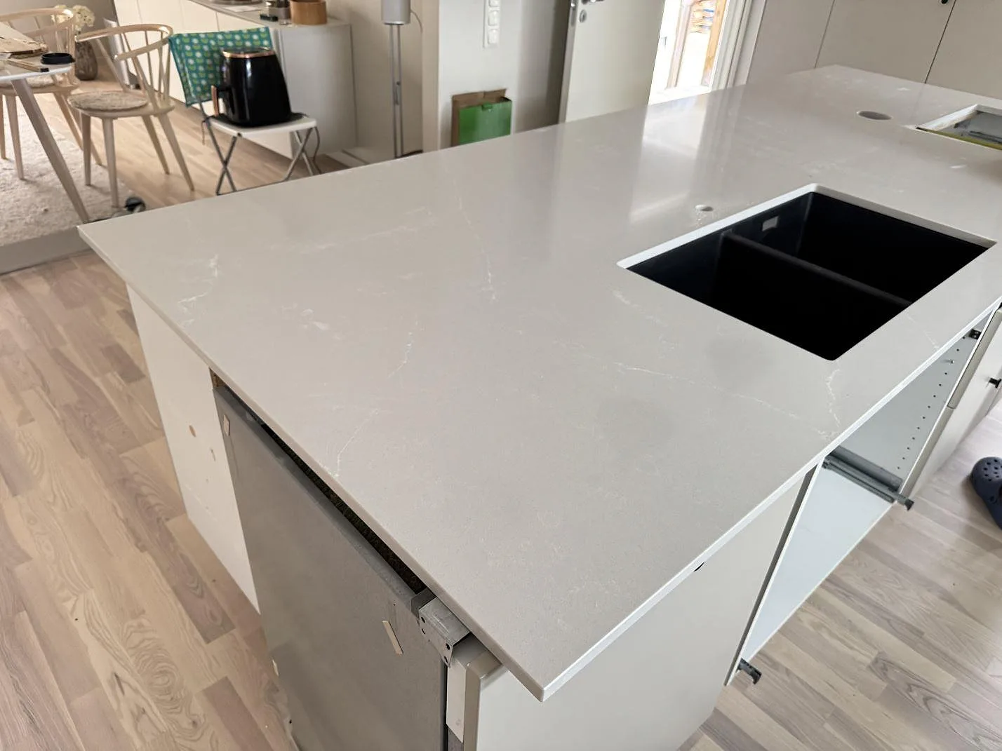 Köksbänkskiva i polerad Silestone Desert Silver, ljus kvartskomposit, med svart diskho och öppna köksstommar under montering i Karlskrona.