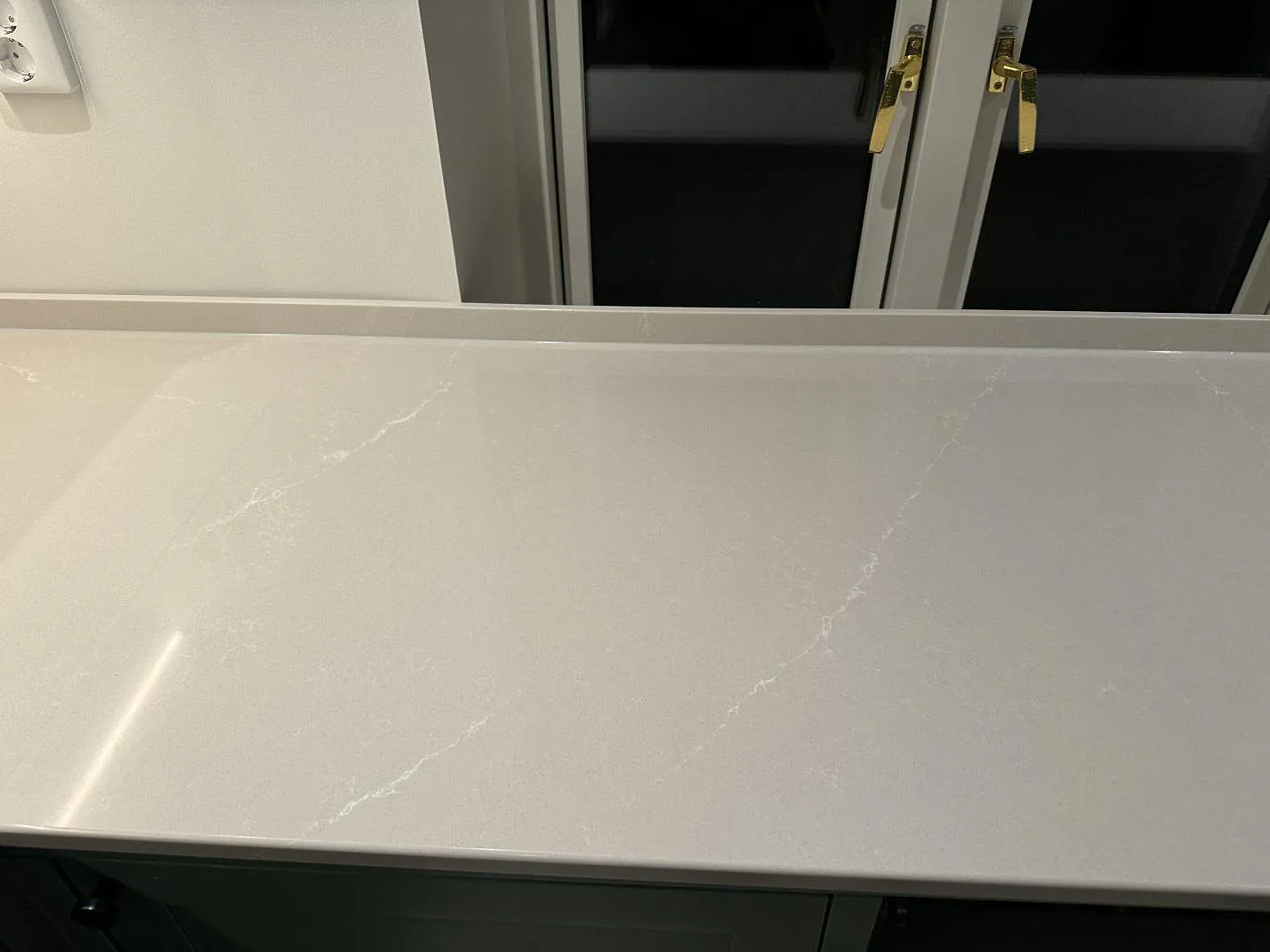 Rak köksbänkskiva i polerad Silestone Desert Silver framför fönster med låg stänkkant i Klagshamn.