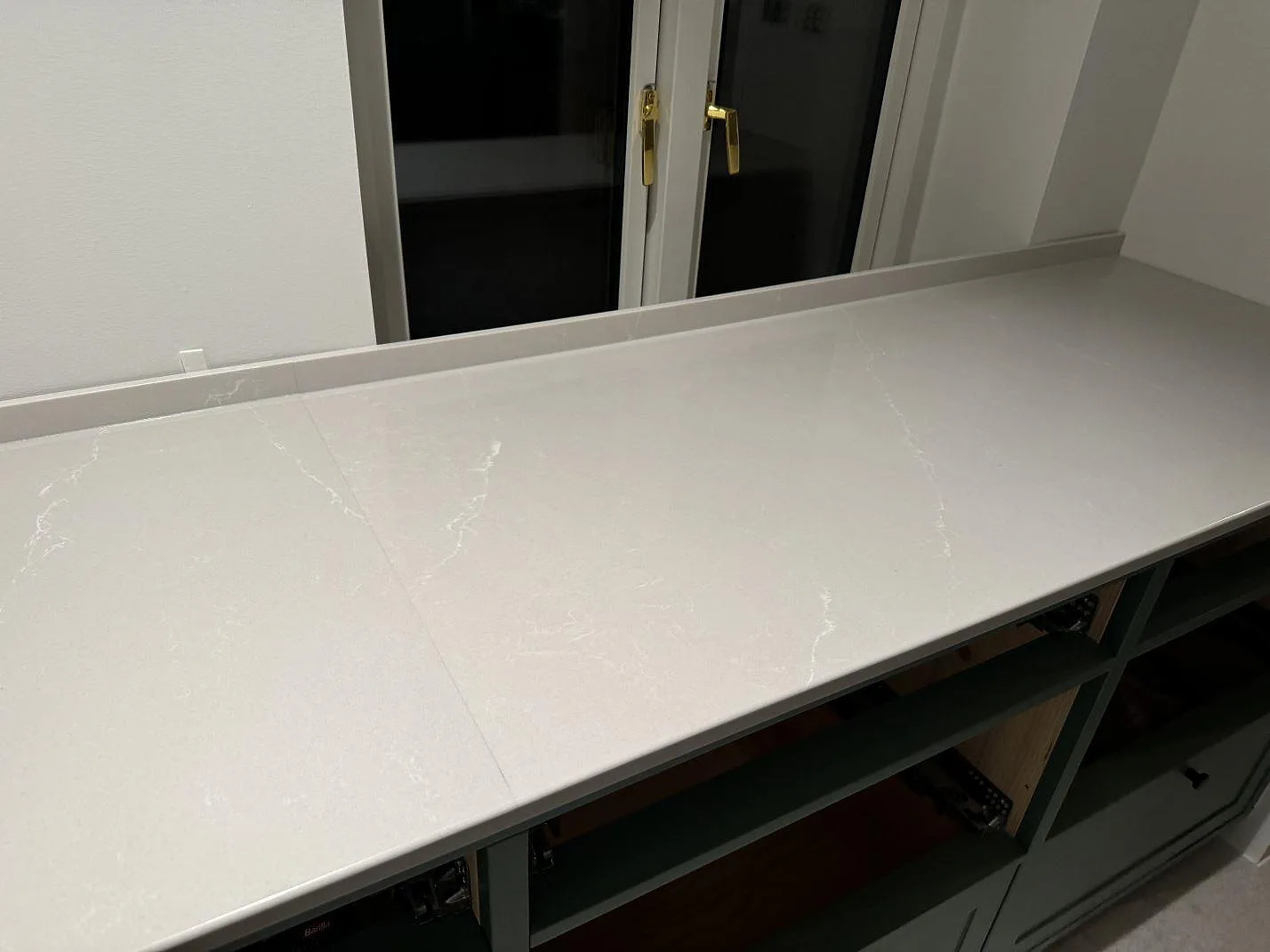 Polerad Silestone Desert Silver längs fönsterväggen, monterad som ljus kompositbänkskiva på öppna köksstommar i Klagshamn.