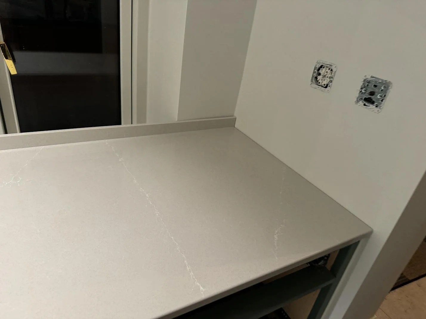 Ändsektion av köksbänkskiva i polerad Silestone Desert Silver med låg stänkkant och öppna eluttag under montering i Klagshamn.