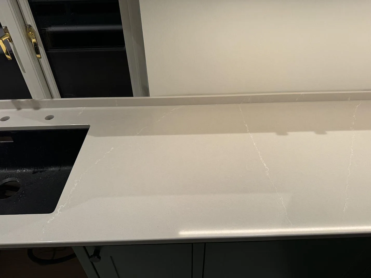 Diskhozon i polerad Silestone Desert Silver med svart diskho, blandarhål och låg stänkkant i ett kök i Klagshamn.