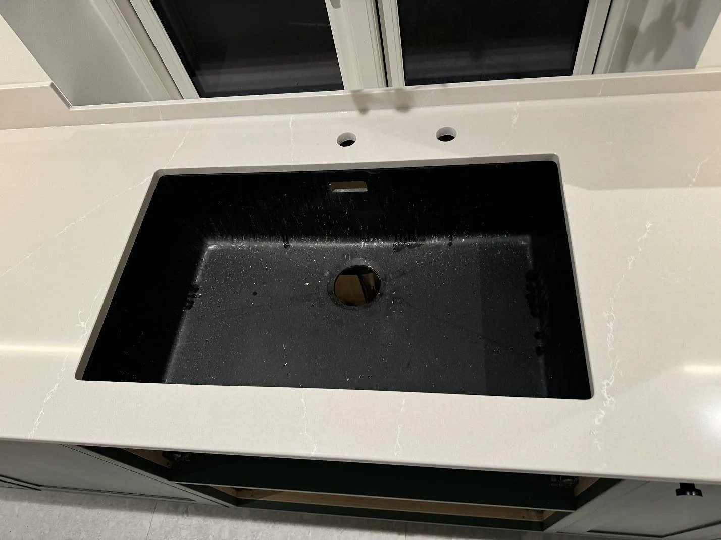 Närbild på svart diskho i en polerad Silestone Desert Silver köksbänkskiva med två blandarhål i Klagshamn.