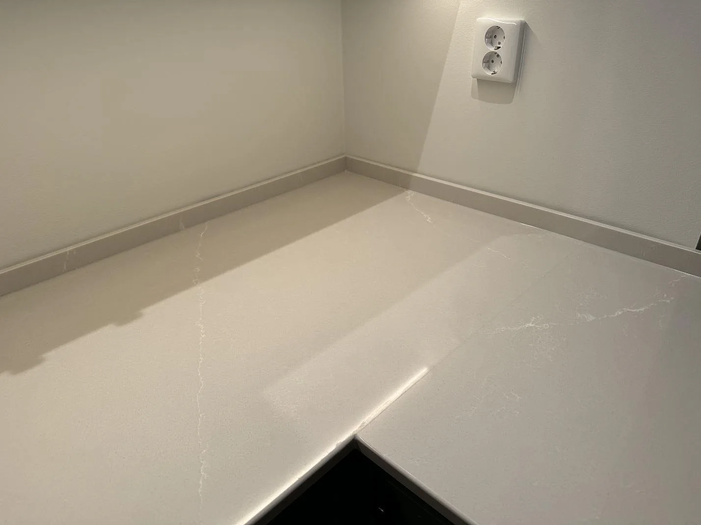 Hörn av polerad Silestone Desert Silver som köksbänkskiva med låg stänkkant och ljus ådring i Klagshamn.