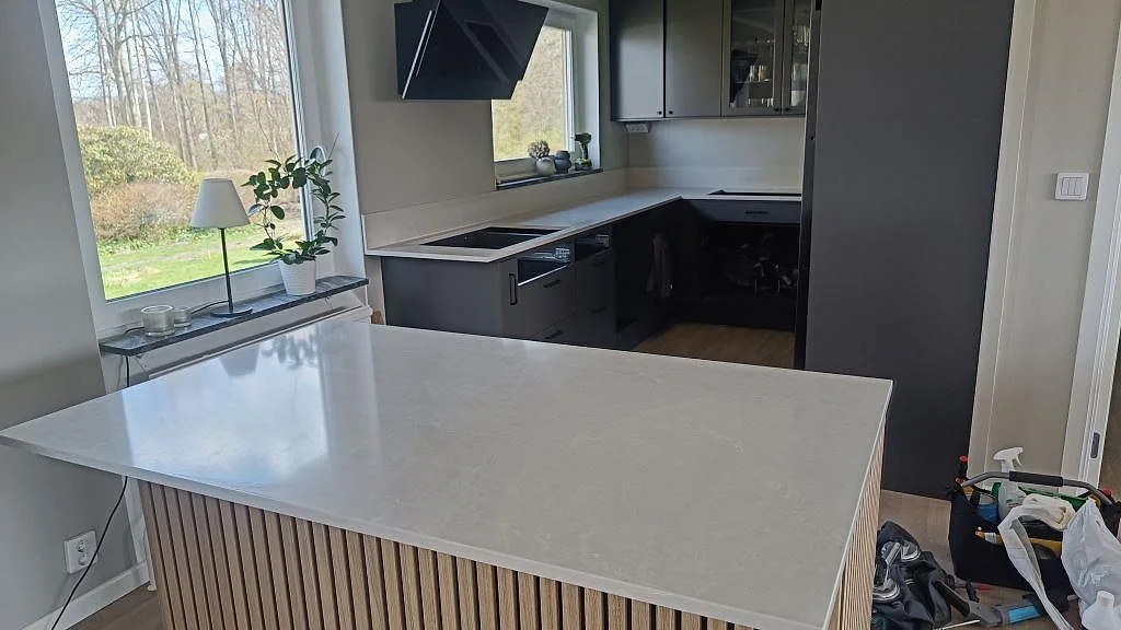Köksbänkskiva och köksö i Silestone Desert Silver, polerad, i ett ljust kök i Lidköping med integrerat stänkskydd och mörka stommar under montering.