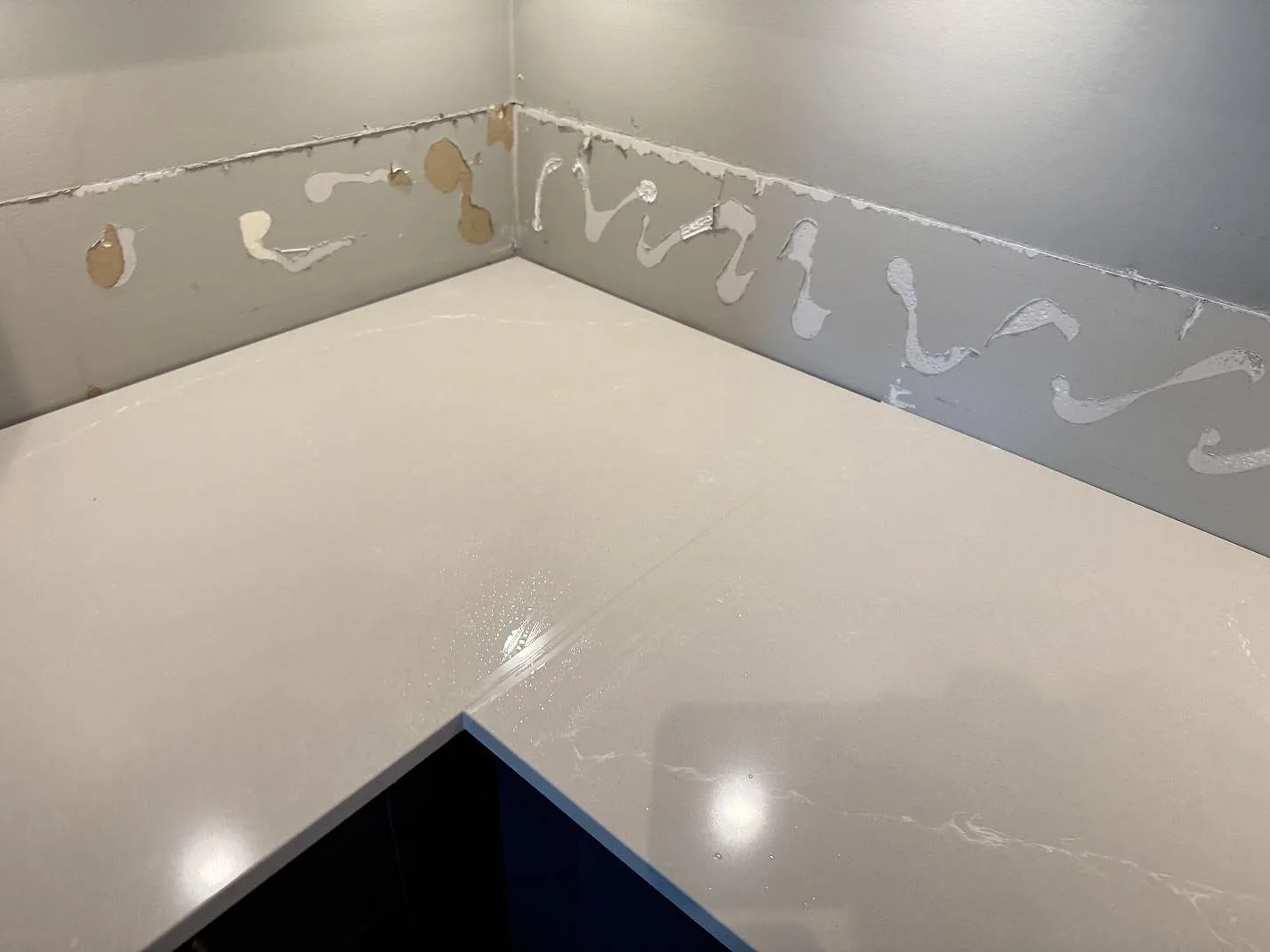 Ljus köksbänkskiva i polerad Silestone Desert Silver vid kökshörn och väggparti under montering i Limhamn.