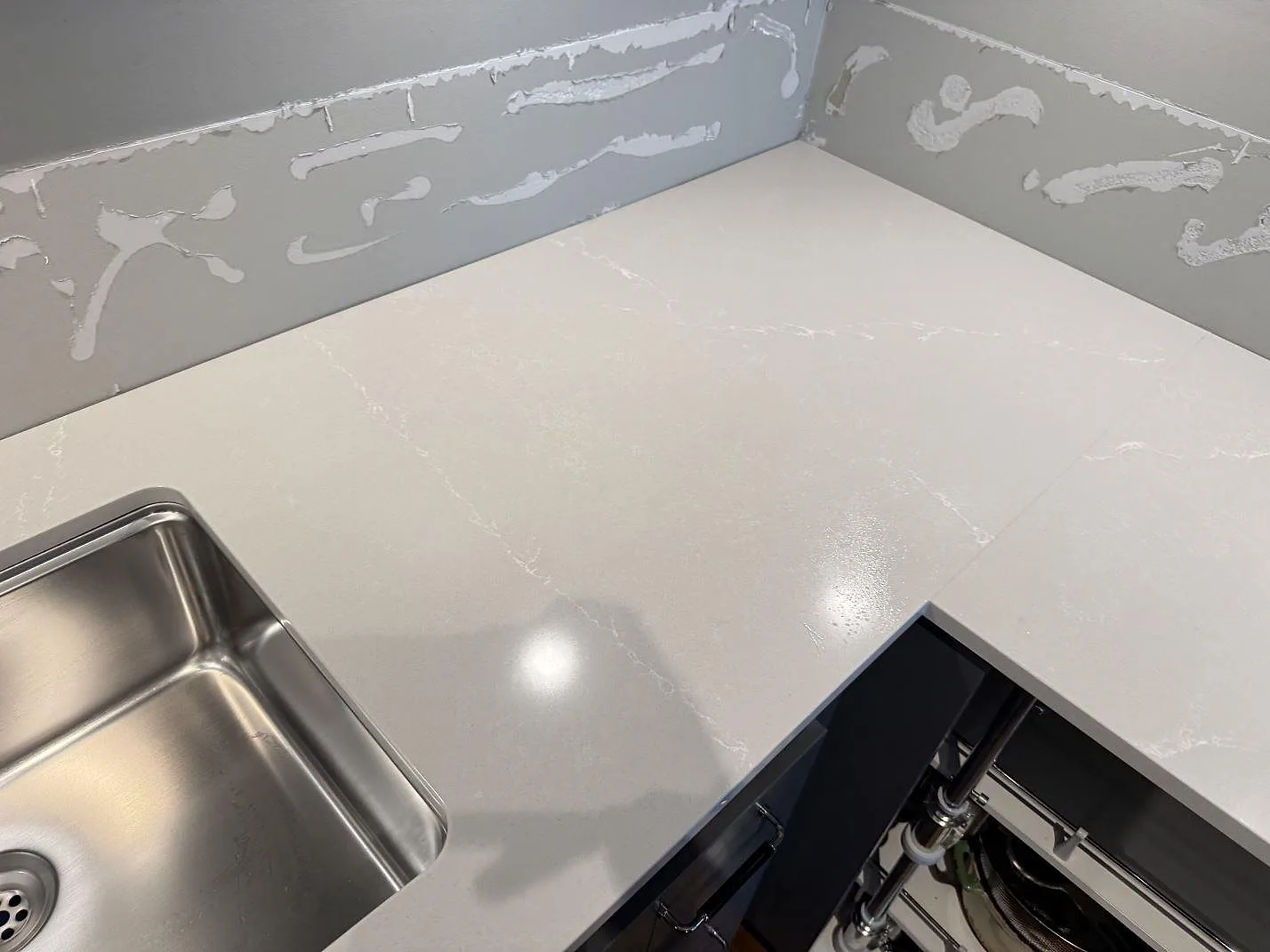 Hörnsektion av köksbänkskiva i polerad Silestone Desert Silver med rostfri diskho och ljusa vener i Limhamn.