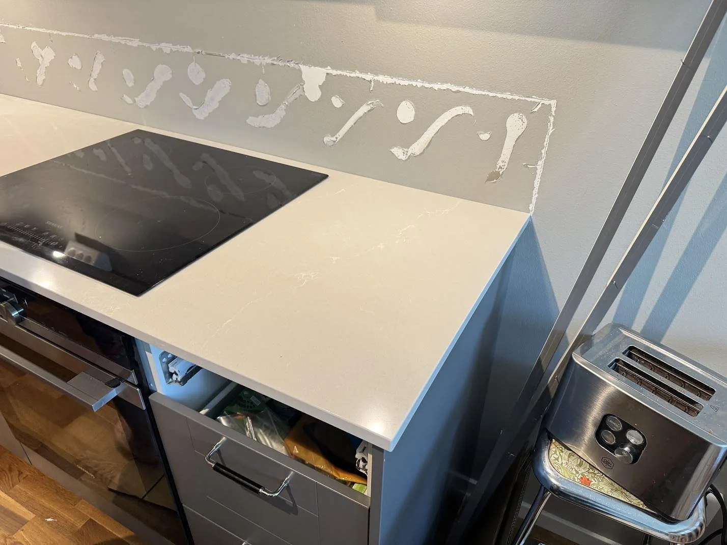 Polerad köksbänkskiva i Silestone Desert Silver vid häll och väggparti i ett kök i Limhamn.