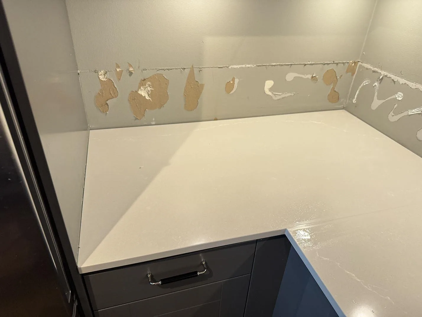 Installerad bänkskiva i polerad Silestone Desert Silver över mörka köksluckor i ett kök i Limhamn.