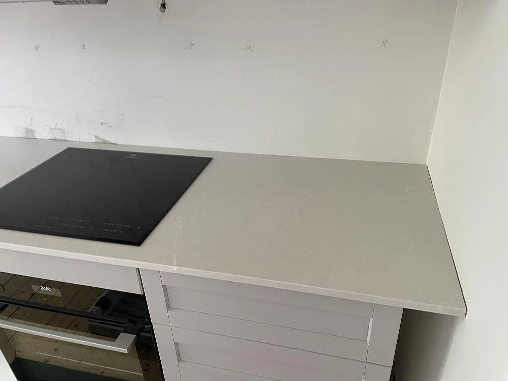 Detalj av Silestone Desert Silver som kompositbänkskiva med svart induktionshäll i ett vitt kök i Lund.