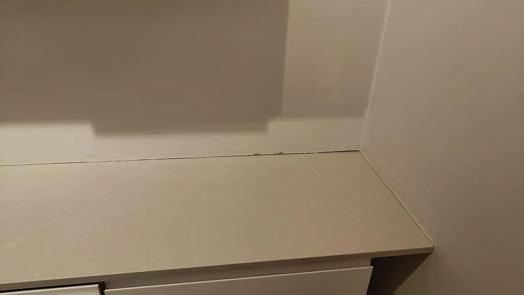 Ändstycke av köksbänkskiva i Silestone Desert Silver, polerad komposit i Lund, monterad mot vägg och skåpstomme.