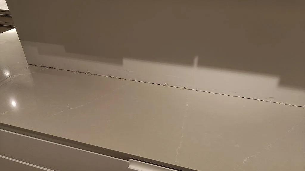 Lång väggnära köksbänkskiva i polerad Silestone Desert Silver komposit i Lund, med diskret ådring i den ljusa ytan.