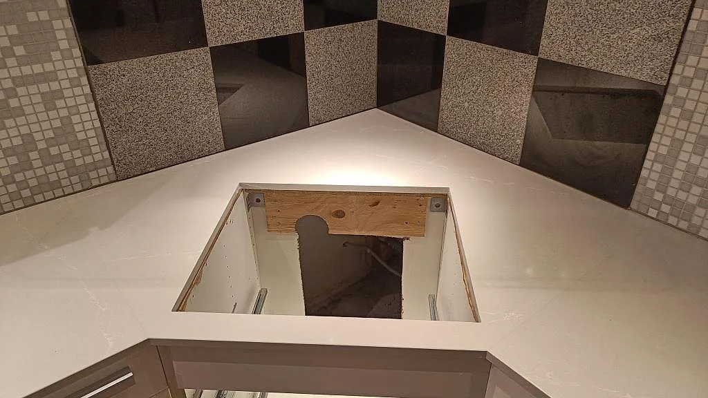 Detalj av Silestone Desert Silver köksbänkskiva, polerad komposit i Lund, med monteringsöppning och kaklad vägg bakom.