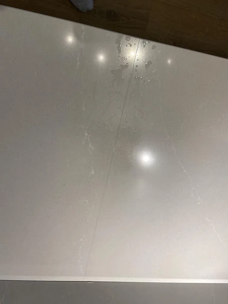 Köksbänkskiva i Silestone Desert Silver, polerad gråbeige kvartskomposit, monterad i ett kök i Malmö med gråröna stommar och waterfall-gavel, fotograferad under montering.