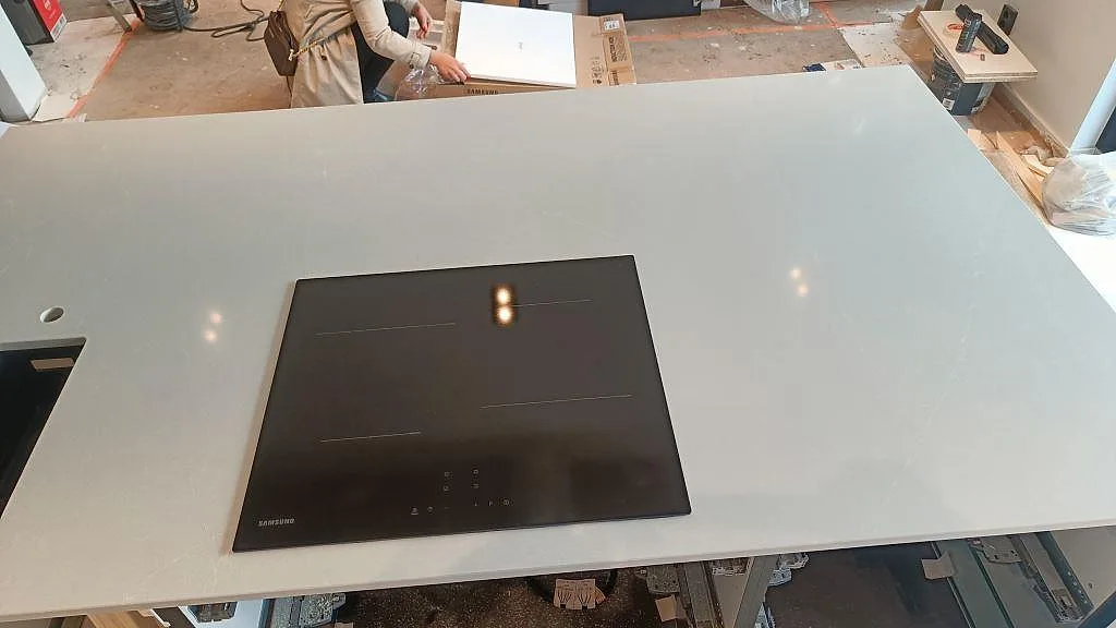 Köksö i polerad Silestone Desert Silver med svart induktionshäll och ljus ådring i ett kök i malmö.