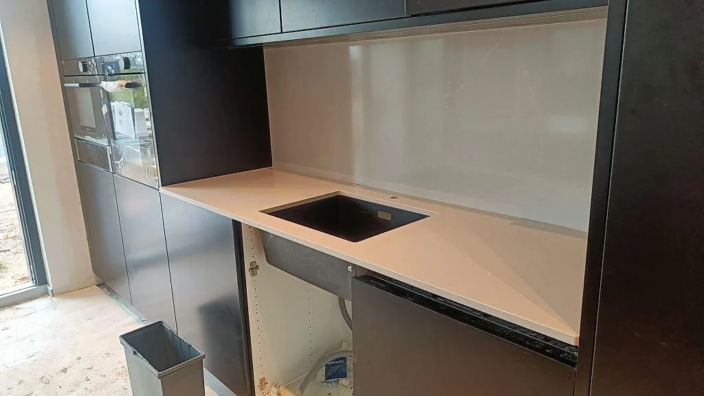 Väggbänk i polerad Silestone Desert Silver med svart diskho och högt stänkskydd i mörkt kök i malmö.