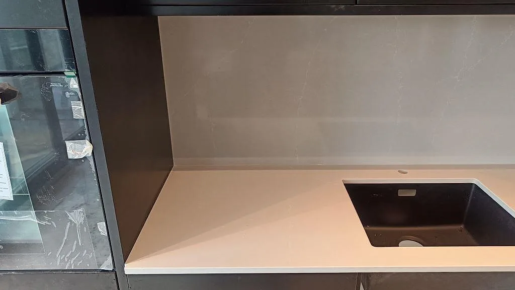 Detalj av polerad Silestone Desert Silver vid svart diskho och ljus stänkskiva mellan mörka skåp i malmö.