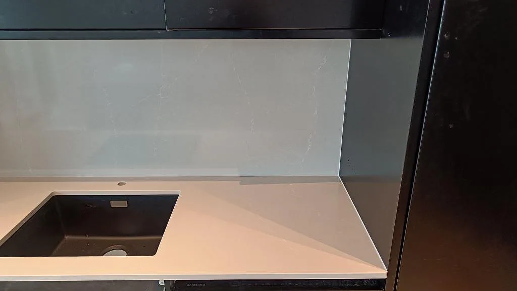 Höger sida av väggbänk i polerad Silestone Desert Silver med svart diskho och högt stänkskydd i malmö.