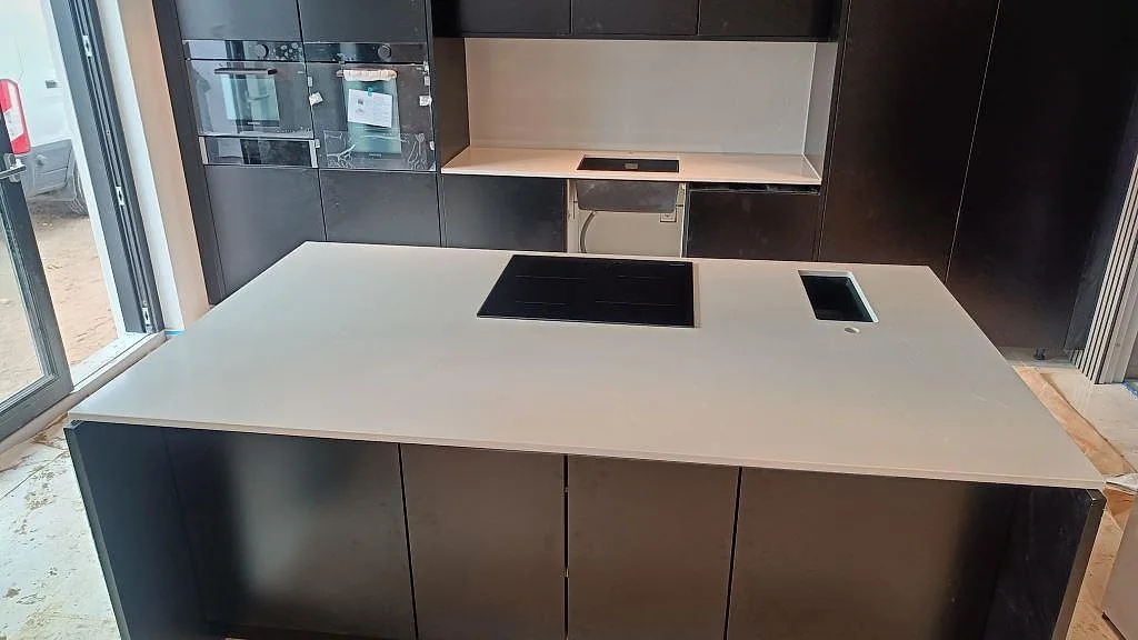 Köksbänkskiva i grå Silestone Desert Silver, polerad, på en köksö med infälld induktionshäll och underlimmad diskho i ett kök i Malmö.