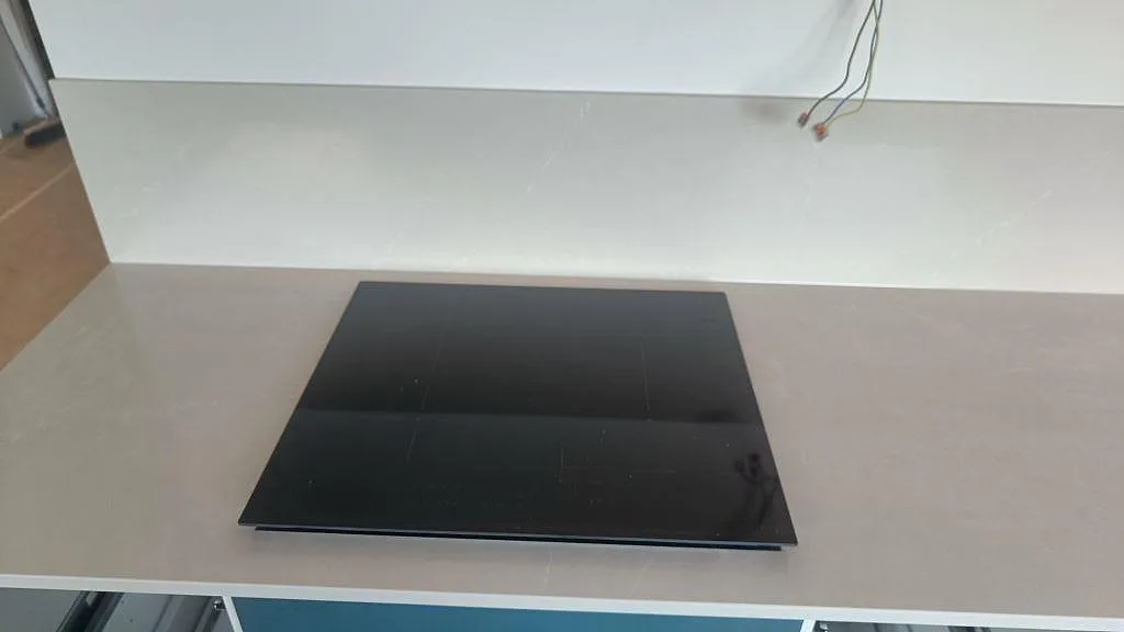 Närbild på svart induktionshäll ovanpå polerad Silestone Desert Silver med stänkskydd bakom i ett kök i Malmö.