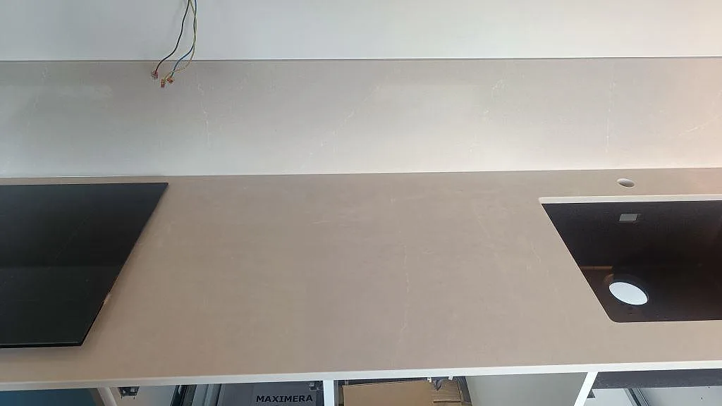 Bänkskiva i polerad Silestone Desert Silver med svart diskho ovanpå stenen, induktionshäll och stänkskydd i Malmö.