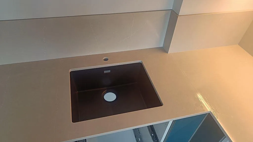 Svart ovanpåliggande kompositdiskho i polerad Silestone Desert Silver med ljus ådring och stänkskydd i ett kök i Malmö.
