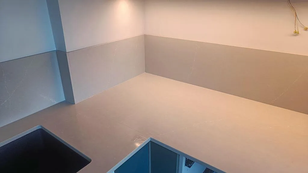 Hörn av polerad Silestone Desert Silver som köksbänkskiva med matchande stänkskydd och blå stommar under montering i Malmö.