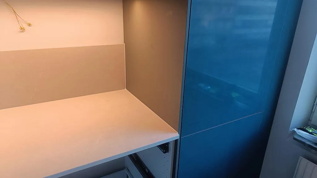 Polerad Silestone Desert Silver som bänkskiva intill blå högskåp och fönster i ett kök under montering i Malmö.
