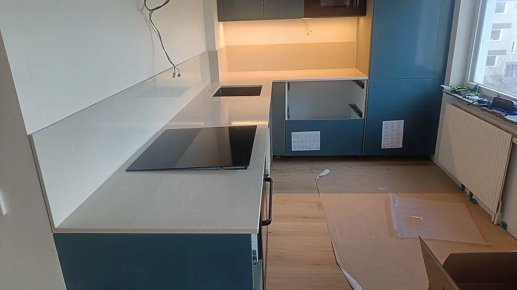 Köksbänkskiva i polerad Silestone Desert Silver med L-form, halvö, induktionshäll och blå köksinredning under montering i Malmö.