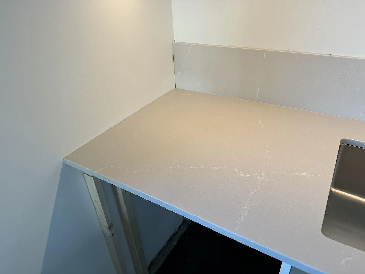 Hörnvy av köksbänkskiva i polerad Silestone Desert Silver med matchande stänkskydd vid diskbänksområdet i Malmö.