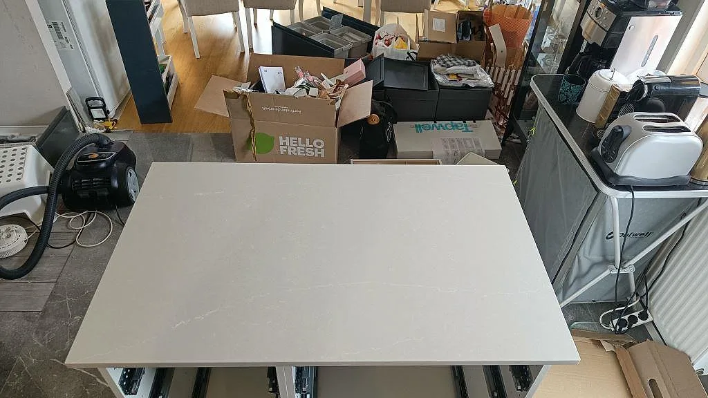 Köksö i varmt greige Silestone Desert Silver, polerad kvartskomposit, monterad i ett kök under installation i Sandared.