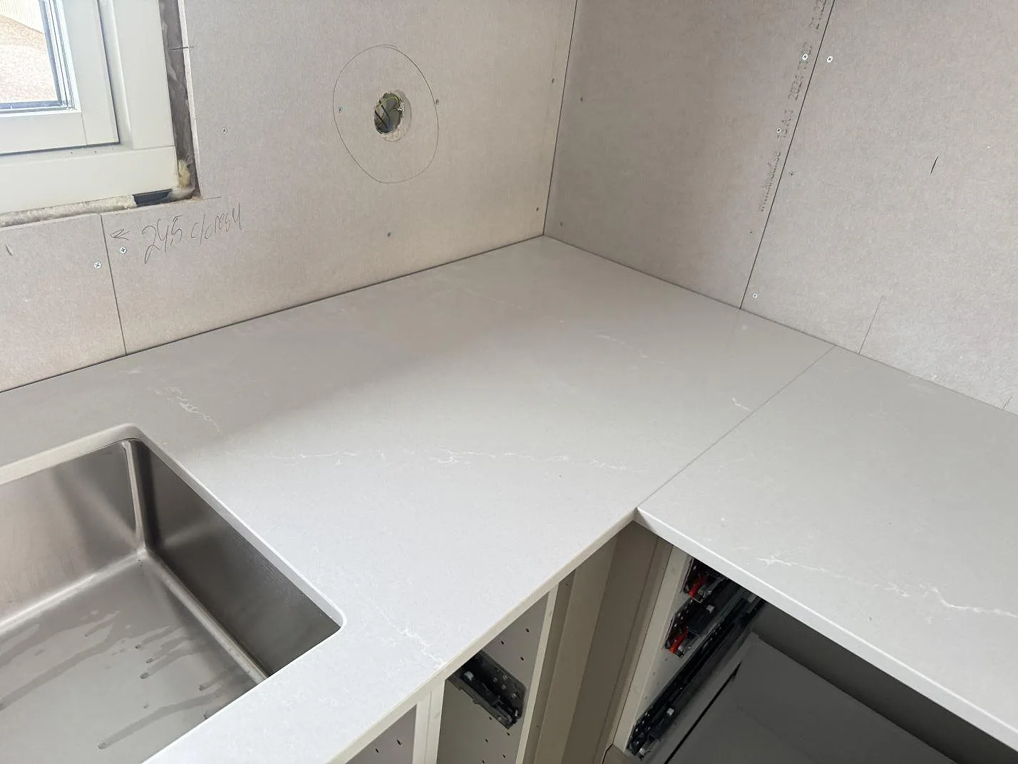 L-formad köksbänkskiva i polerad Silestone Desert Silver, komposit, med diskho och ljus ådring i Sandared.