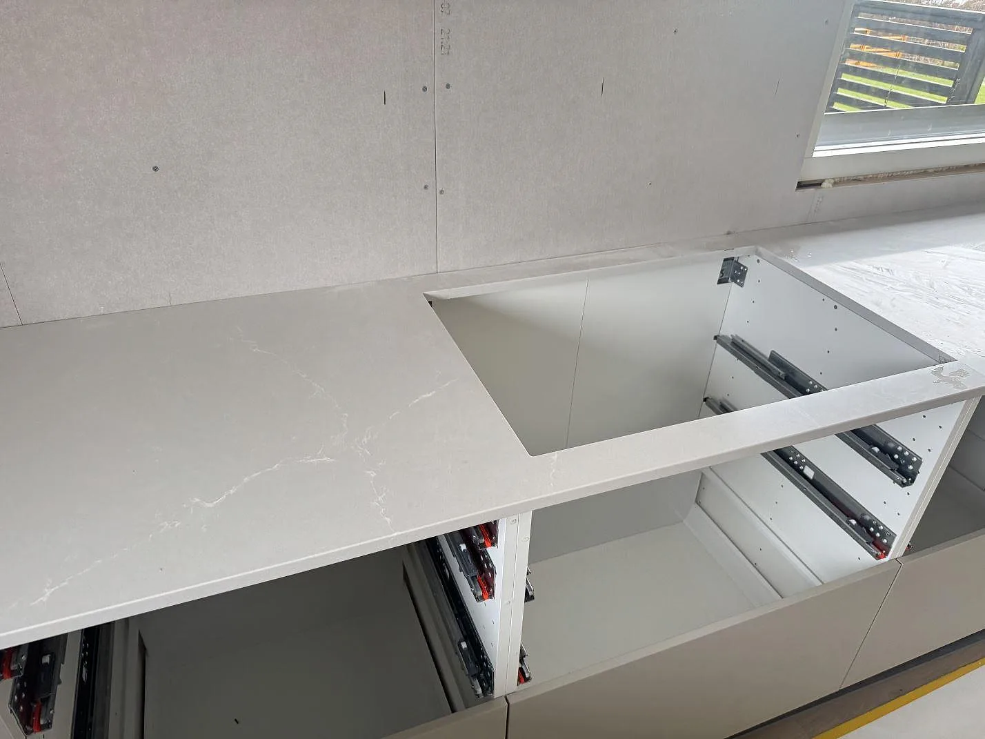 Köksbänkskiva i polerad Silestone Desert Silver, komposit, med rektangulär öppning i öppna stommar i Sandared.