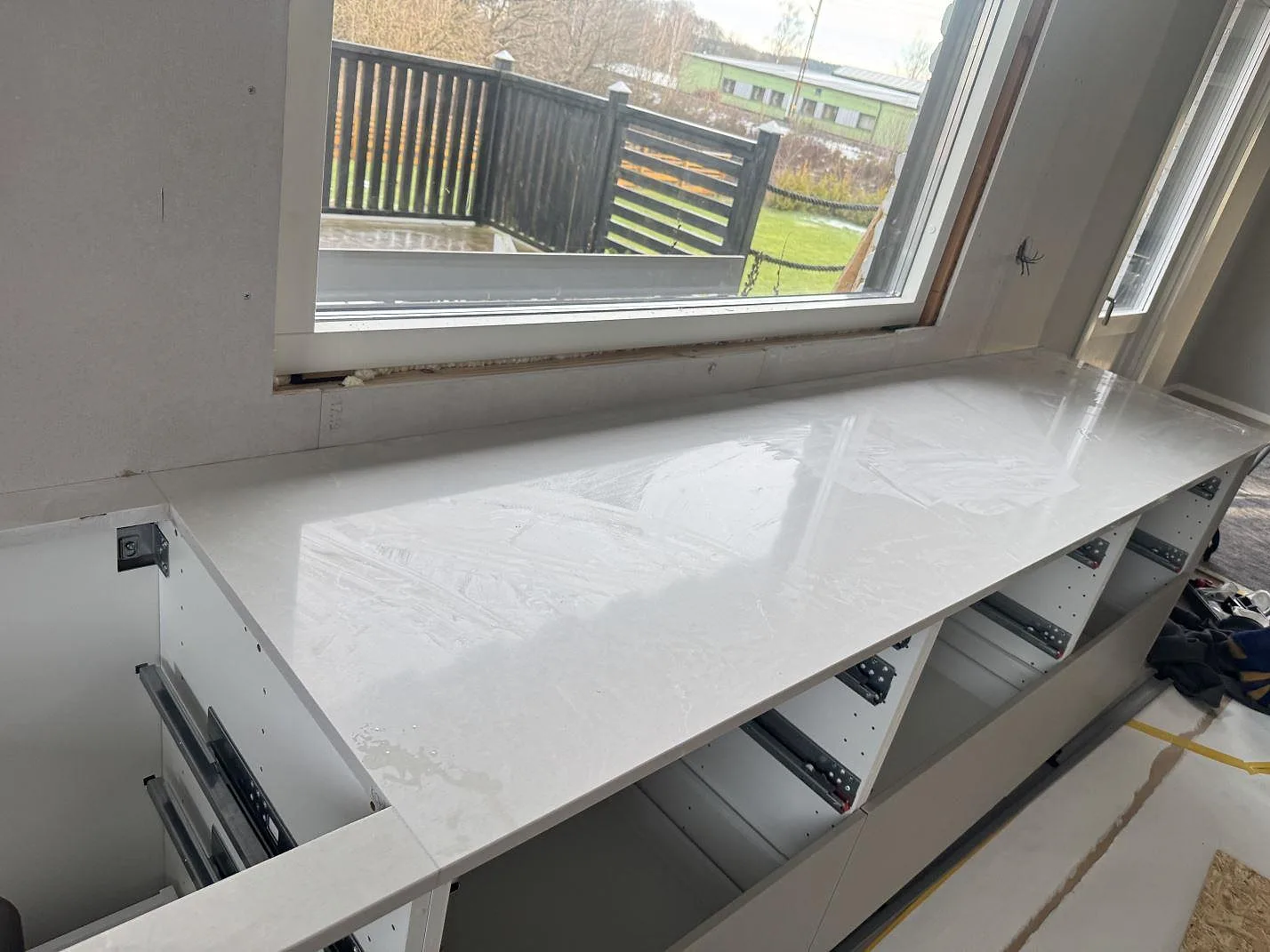 Lång köksbänkskiva i polerad Silestone Desert Silver, komposit, under fönster med öppna köksstommar i Sandared.