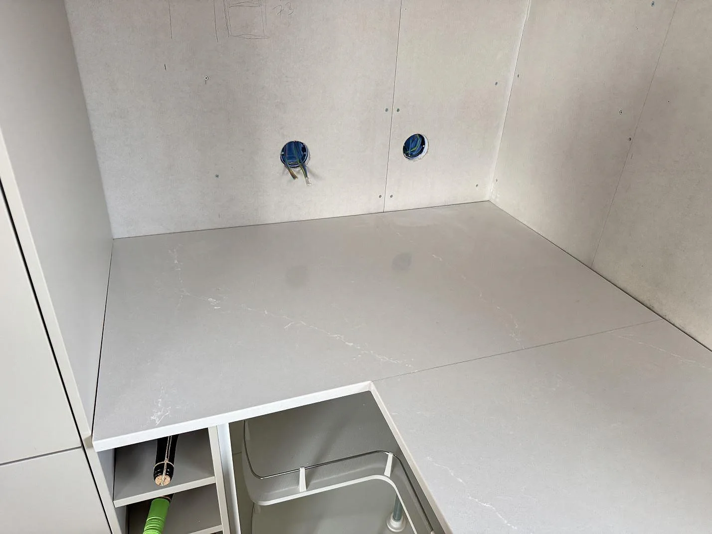 Hörnvy av köksbänkskiva i polerad Silestone Desert Silver, komposit, under montering i Sandared.