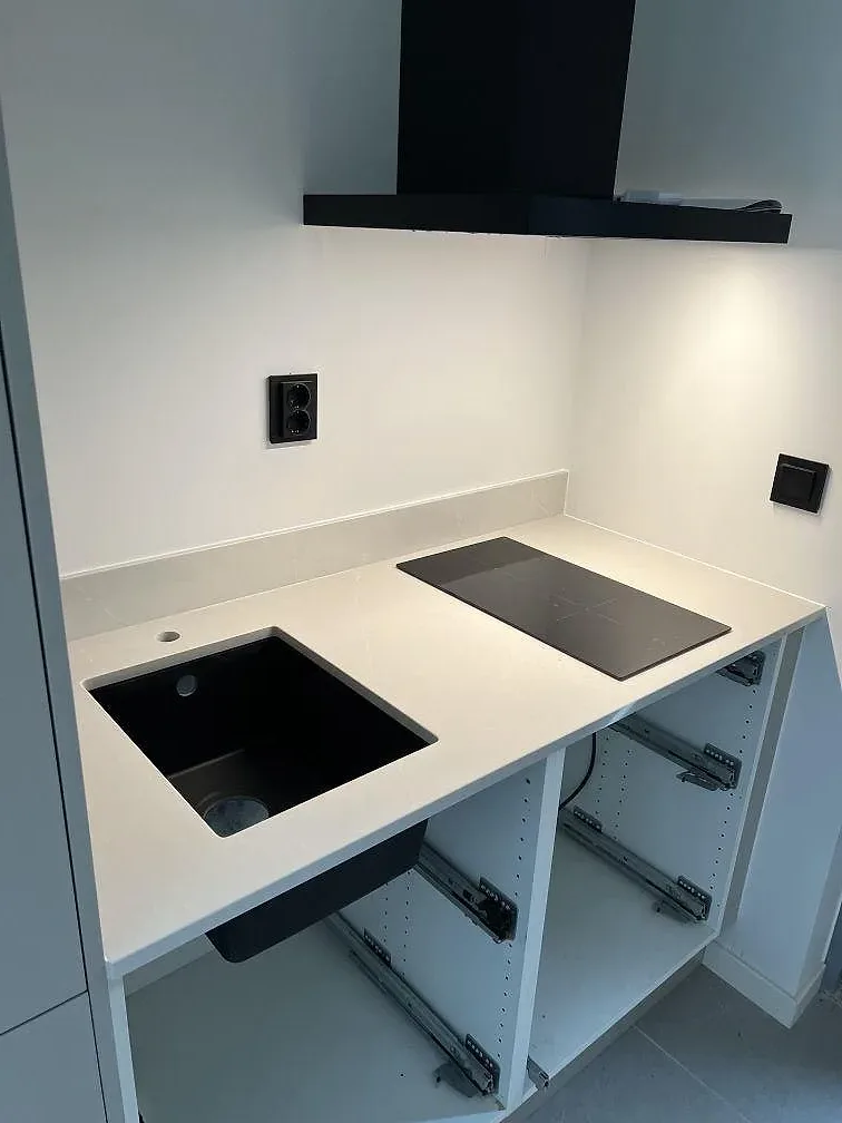 Köksbänkskiva i ljus Silestone Desert Silver, polerad, med svart diskho och svart induktionshäll i ett kök i Skanör.