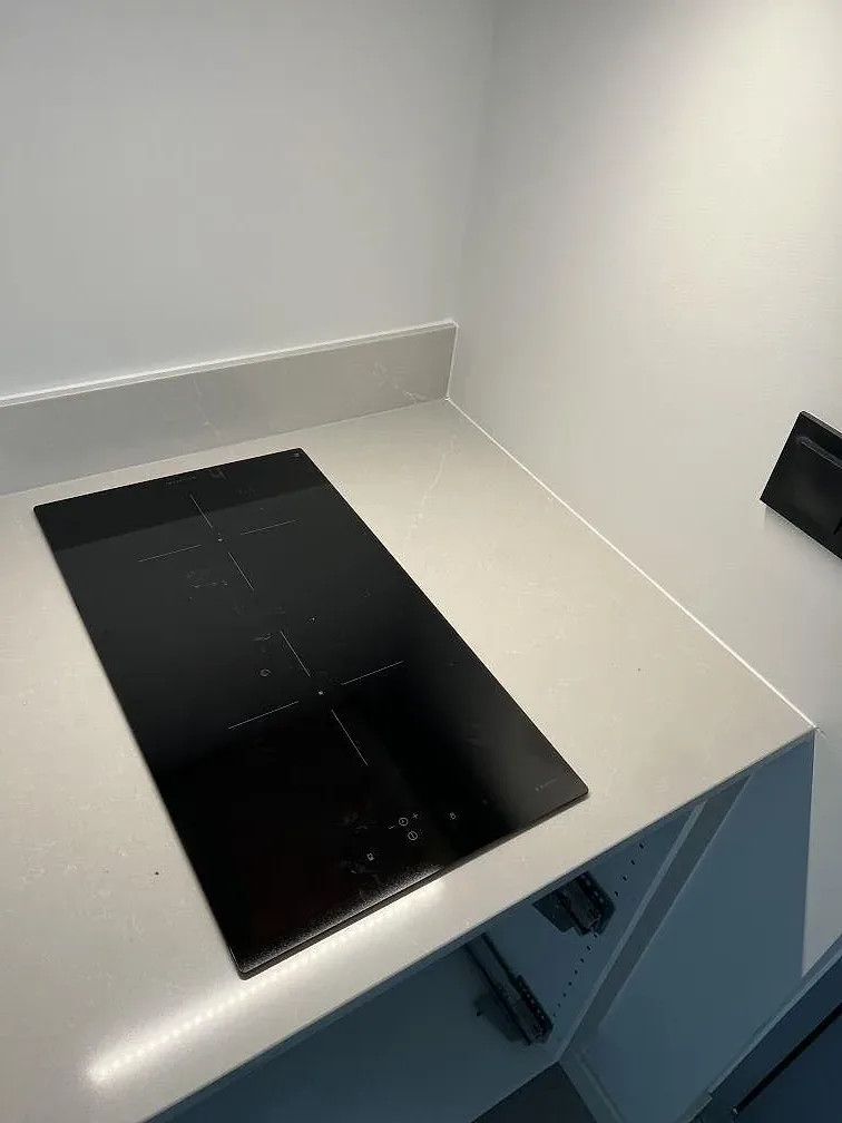 Polerad köksbänkskiva i Silestone Desert Silver med svart induktionshäll och uppvikt stänkkant i Skanör.