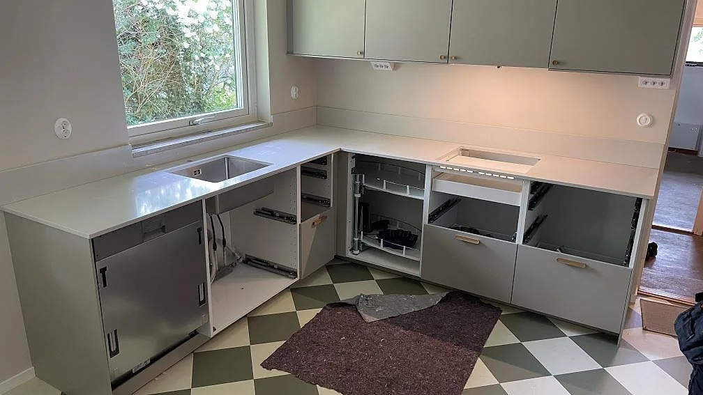 L-formad köksbänkskiva i polerad Silestone Desert Silver, kvartskomposit, med låg stänkkant och rostfri diskho i ett kök i Skanör.