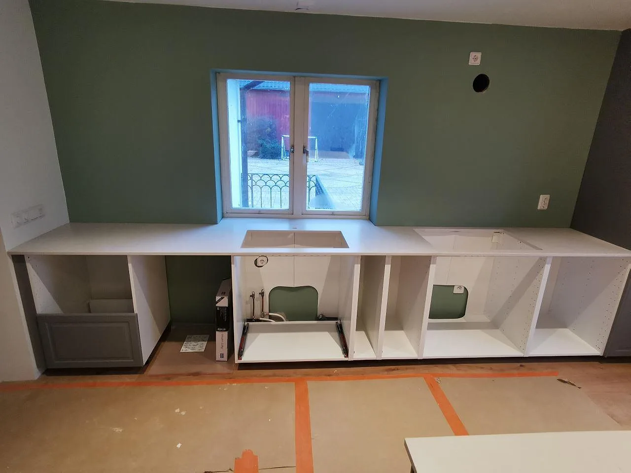Bänkskiva i Silestone Desert Silver längs väggen med fönsterbänk och urtag för diskho och häll i ett kök i Skivarp.