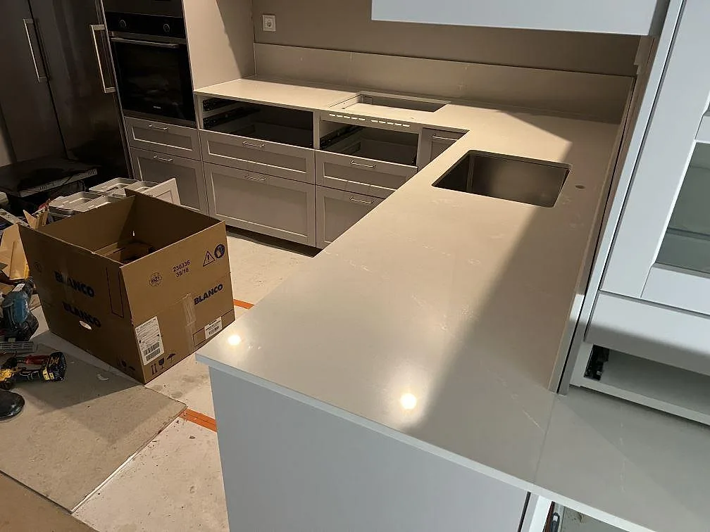 Polerad Silestone Desert Silver som köksbänkskiva och avställningsyta med urtag för häll, diskho och låg stänkkant under montering i Solna.