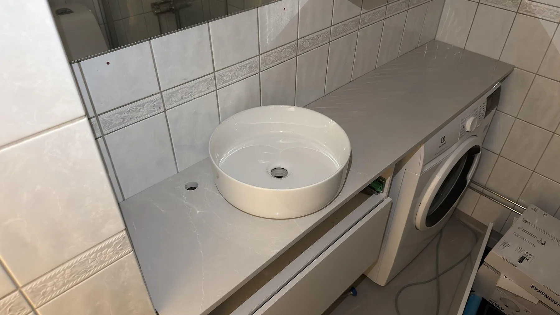 Bänkskiva i polerad Silestone Desert Silver med ovanpåliggande tvättställ och grå ådring i Stockholm.