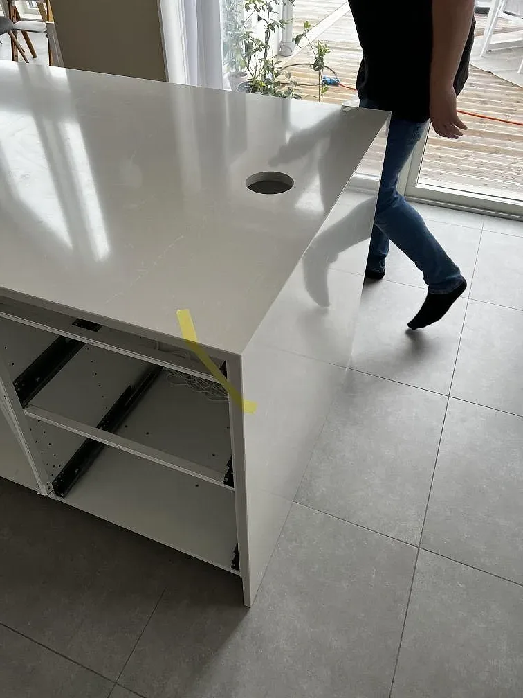 Polerad köksö i Silestone Desert Silver med rund öppning och öppna vita köksstommar under montering i Svedala.