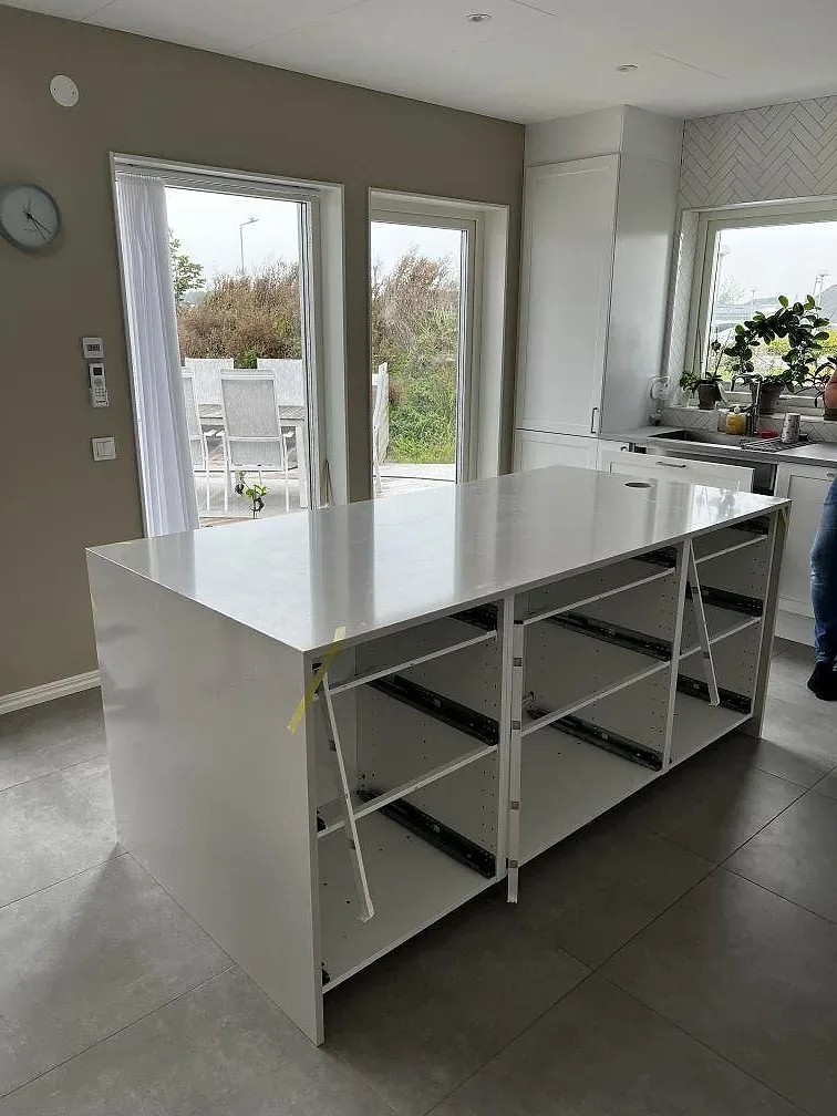 Köksbänkskiva i ljus Silestone Desert Silver, polerad komposit, på en köksö med vita stommar och stora fönster i Svedala.